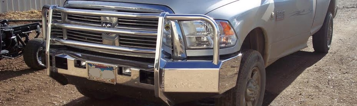 A close-up of an aluminum truck bumper on a Dodge Ram pickup truck parked on a dirt lot.