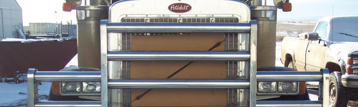 Close-up of a semi truck aluminum bumper on a Peterbilt semi truck in a truck yard with a pickup …