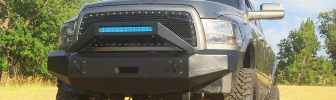 A black pickup truck with a custom TDS aluminum bumper on a grass field clearing with trees around.