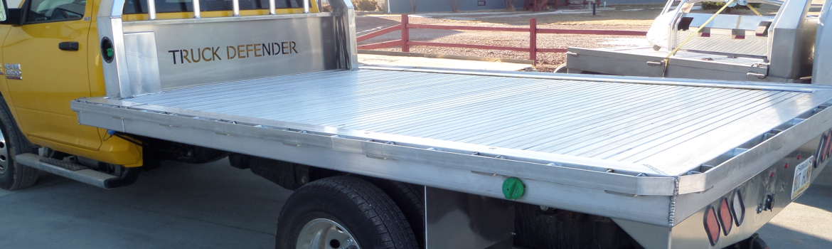 Silver aluminum flatbed on a yellow Dodge Ram pickup truck parked outside of a house.